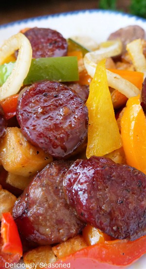A close up photo of smoked sausage, bell peppers, onions, and potatoes.