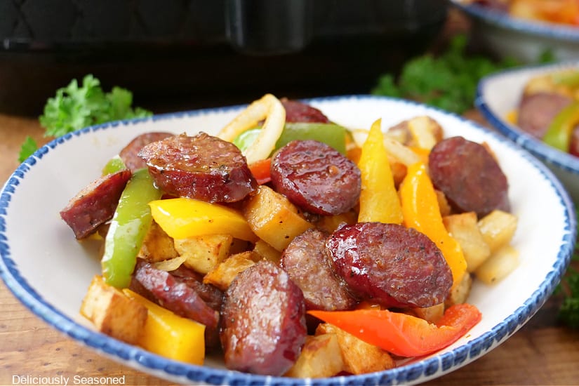 A horizontal photo of a white bowl with blue trim with a serving of peppers, sausage and potatoes.