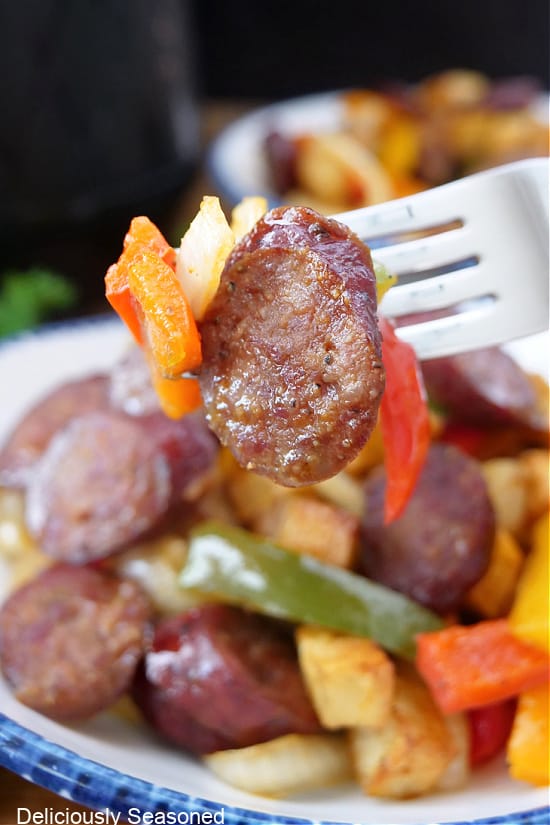 A close up of a bite of smoked sausage, peppers and onions on a fork.