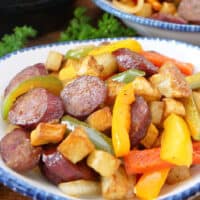 A white bowl with blue trim filled with air fried sausage, peppers, and potatoes.