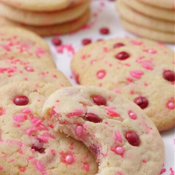 A white surface with a couple dozen Valentine sugar cookies on it.