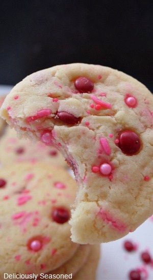 A sugar cookie with a bite taken out of it held up showing the sprinkles and red M&Ms.