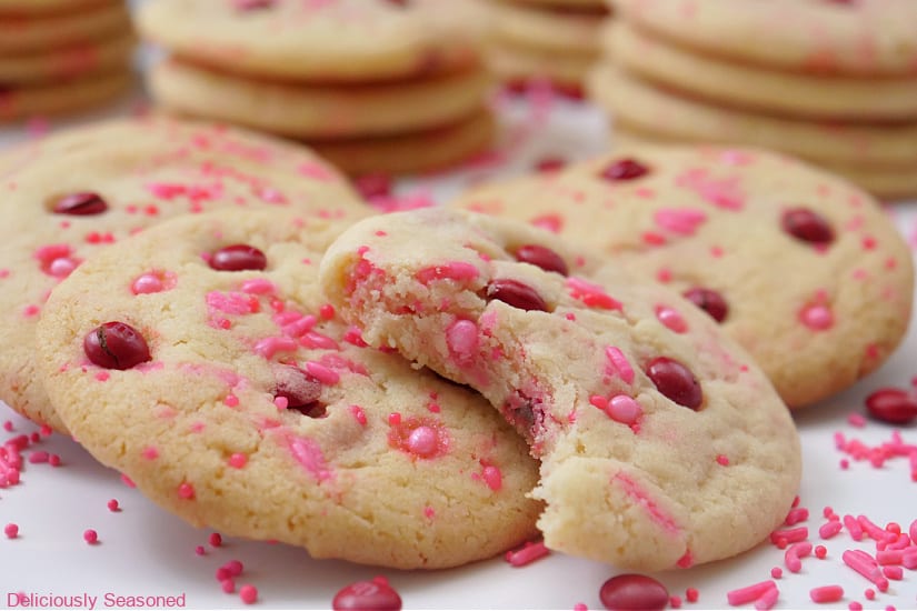 A horizontal photo of a close up of a few sugar cookies on a white surface with a bite taken out of one of the cookies.