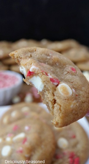 A white chocolate chip cookie with peppermint chips in it and a bite taken out of it.