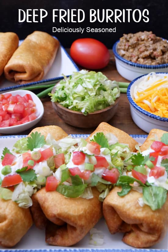 A wood surface with deep fried burritos on white plates with blue trim, with lettuce, tomatoes, shredded cheese, and ground beef mixture in the background.