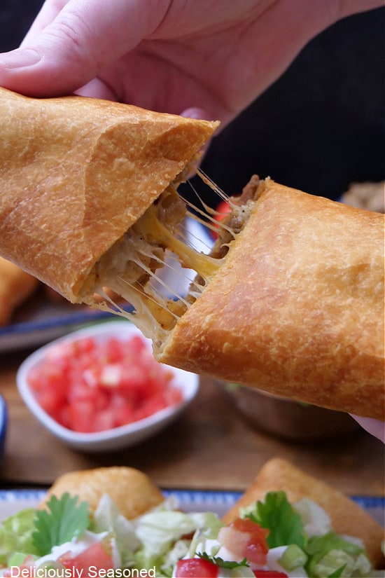 A deep fried burrito cut in half and being pulled apart showing the gooey melty cheese.
