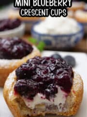 A close up of a crescent dough cup filled with sweet cream cheese and topped with blueberries.