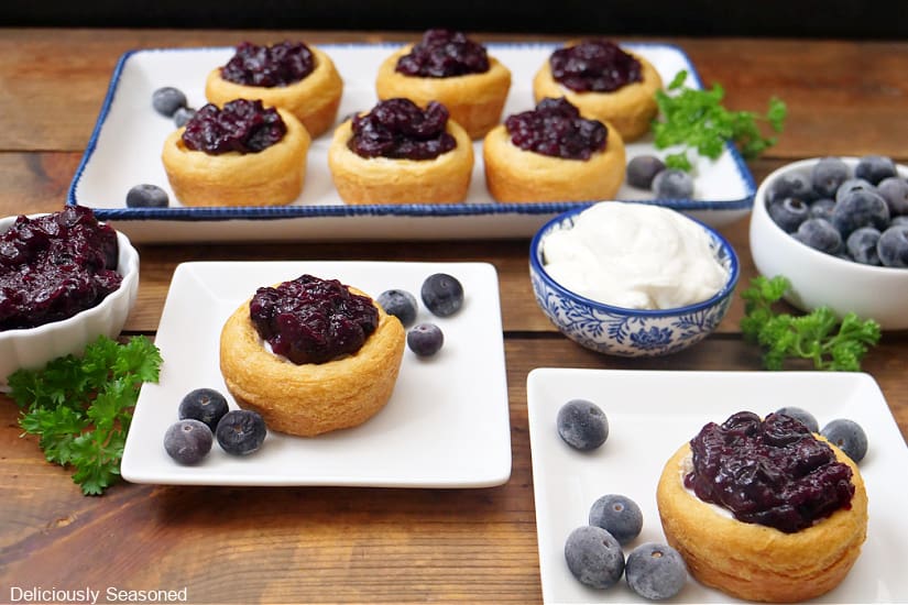 A horizontal photo of a wood surface with whit plates with mini blueberry cups on them.