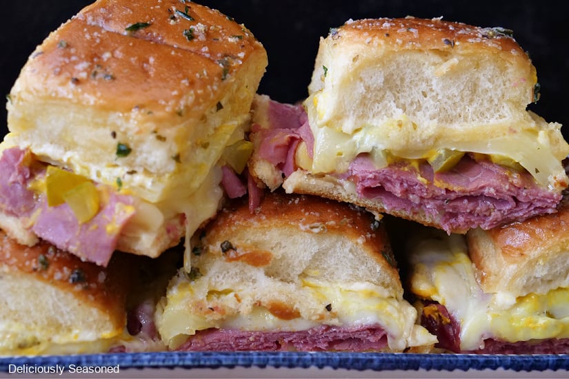 Two pastrami sliders stacked on top of 3 sliders on a white plate with blue trim.