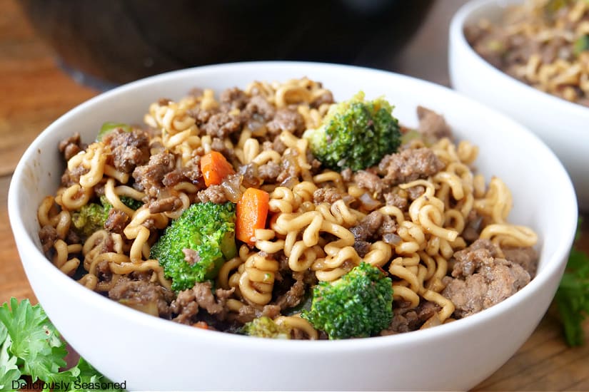 A horizontal photo of a white bowl filled with a serving of ramen noodles with ground beef, broccoli, and carrots.