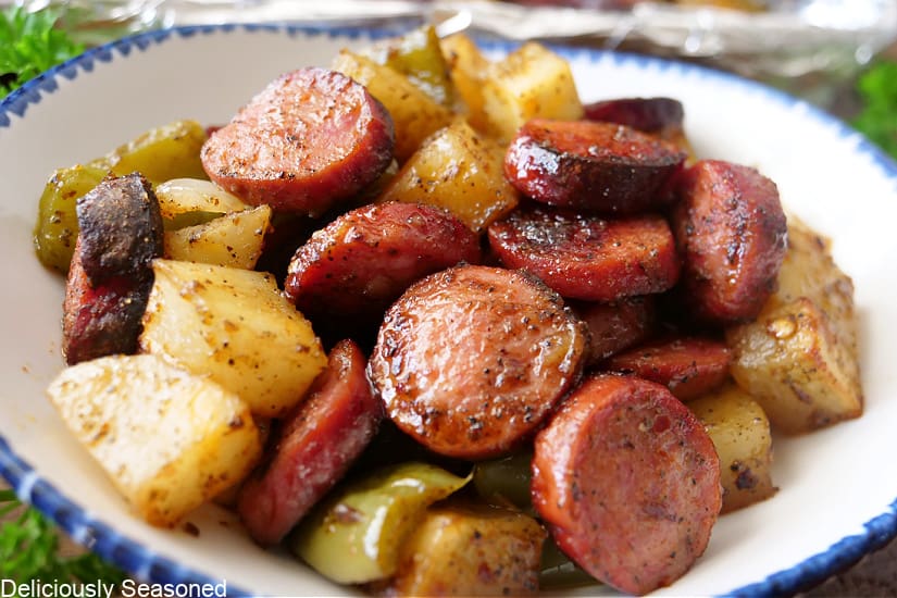 A horizontal photo of a white bowl with blue trim filled with sausage and potatoes.