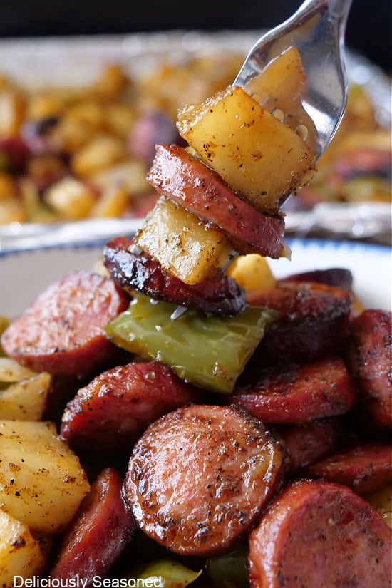 A close up of a fork with a bite of sausage, potatoes, and bell pepper.