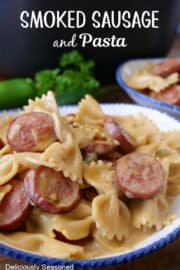 A white bowl with blue trim filled with a serving of smoked sausage and bow tie pasta in a creamy sauce.