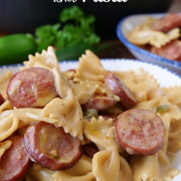 A white bowl with blue trim filled with a serving of smoked sausage and bow tie pasta in a creamy sauce.