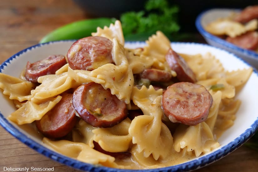 A white bowl with blue trim filled with a serving of creamy bow tie pasta and smoked beef sausage.