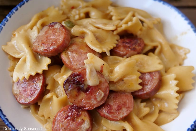 A horizontal photo of a white bowl with blue trim filled with a serving of pasta and sliced smoked sausage.
