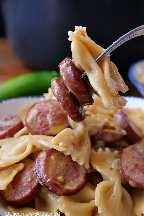 A close up photo of a fork with a bite of bow tie pasta and sliced smoked sausage on it.