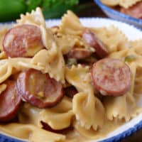 A close up of a bowl filled with smoked sausage and bow tie pasta.