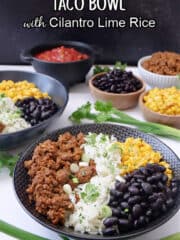 A white surface with two black bowls filled with taco meat, white rice, corn, black beans and cheese, with little bowls in the background filled with the same ingredients.