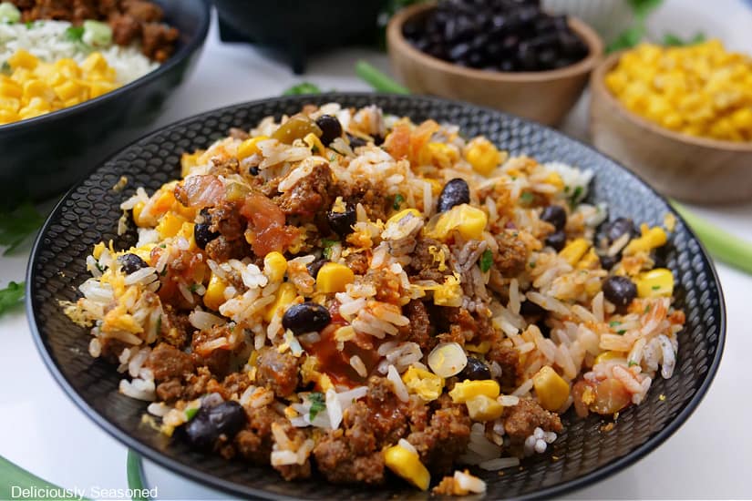 A horizontal photo of a black bowl with ground beef, corn, beans, cheese, and rice.
