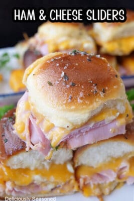 A close up of three ham and cheese sliders with more sliders in the background.
