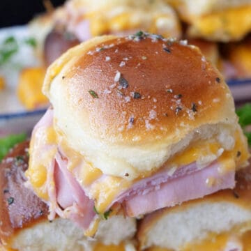 A close up of three ham and cheese sliders with more sliders in the background.