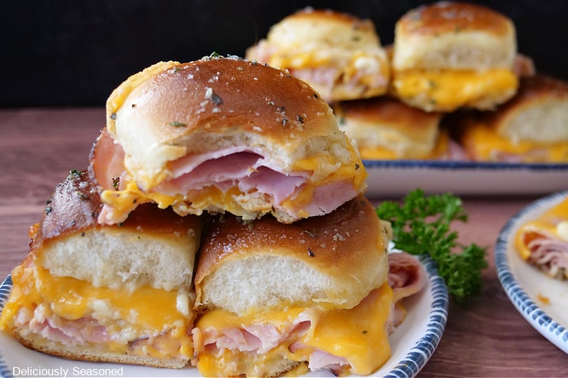 A horizontal photo of ham and cheese sliders on white plates with blue trim.