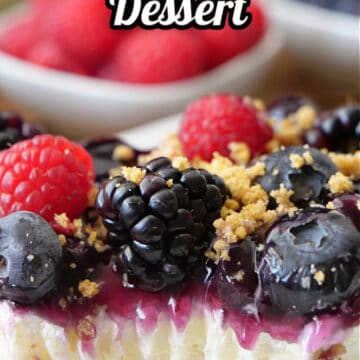 A close up piece of mixed berry dessert which has a graham cracker crust, sweet cream cheese layer and fresh berries on top.