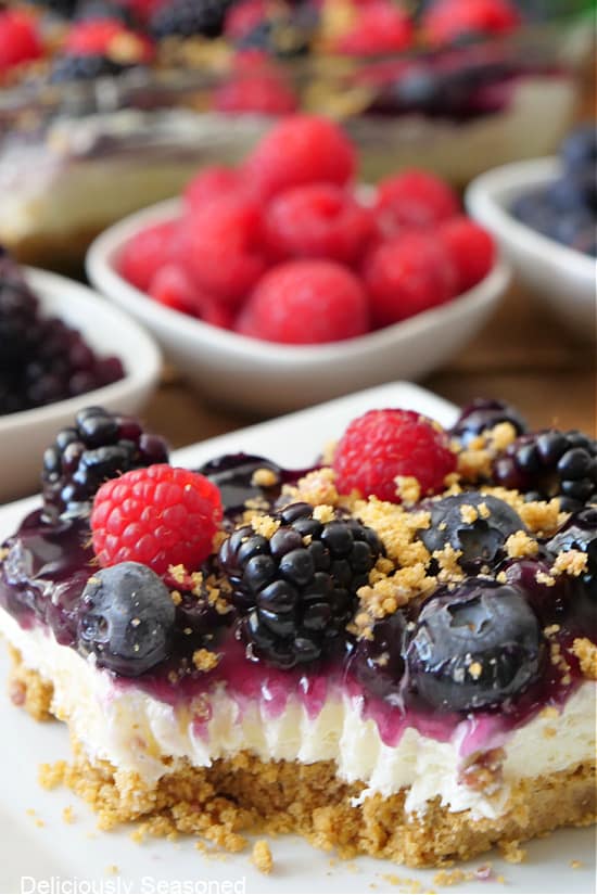 A slice of mixed berry dessert on a white plate with fresh berries in the background.