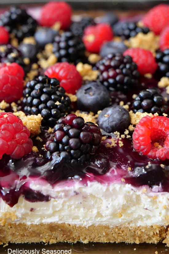 A close up of a graham cracker crust, a sweet cream cheese mixture and topped with fresh berries.