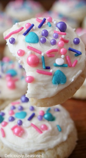 A close up of a frosted sugar cookie with white frosting and candy sprinkles on top, with a bite taken out.