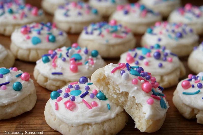 A horizontal photo of a wood surface with over a dozen frosted sugar cookies with cany sprinkles on top.