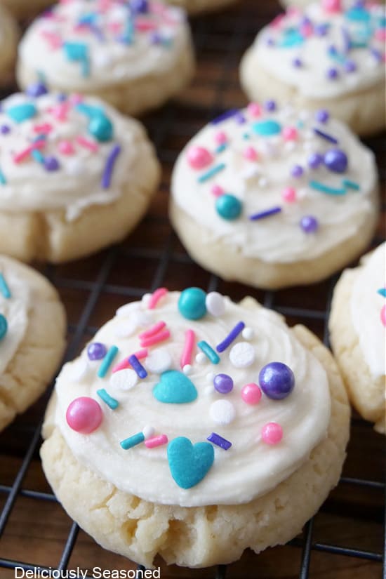 A close up of a few soft frosted sugar cookies on a white rack.