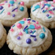 A close up of a few sugar cookies with white frosting and colorful sprinkles on top.