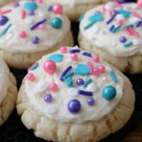 A close up of a few sugar cookies with white frosting and colorful sprinkles on top.