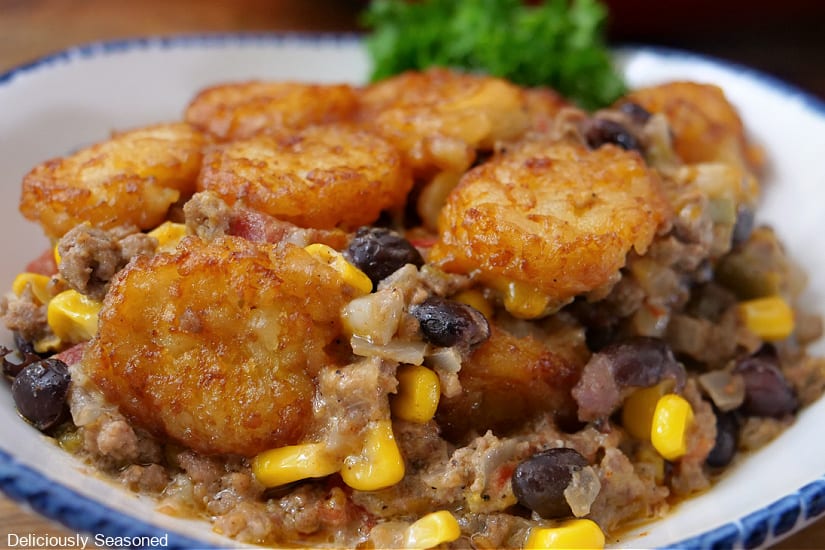 A horizontal photo of a serving of Southwest tater tot casserole in a white bowl with blue trim.