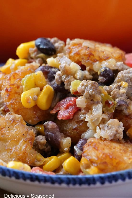A close up of a serving of southwest tater tot casserole in a white bowl with blue trim.
