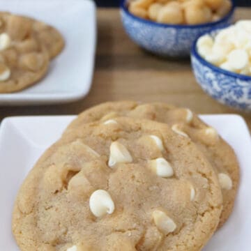 A white small plate with two white chocolate macadamia nut cookies on it.