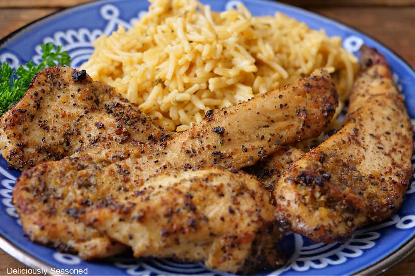 A horizontal photo of a blue plate with baked lemon pepper chicken strips and rice on the plate.