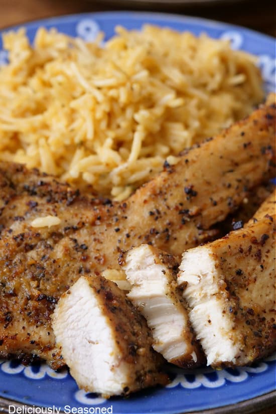 A close up of lemon pepper chicken strips and rice on a blue plate.