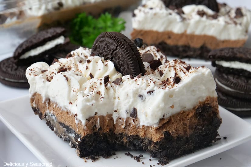 A horizontal photo of a chocolate dessert bar with an Oreo crust, a chocolate cream layer and homemade whipped cream.