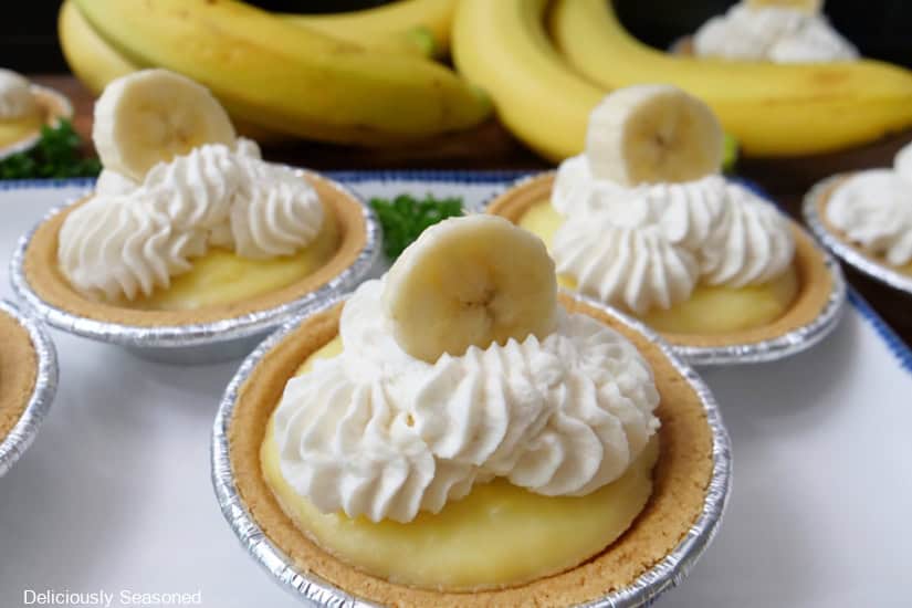 A horizontal photo of mini banana cream pies on a white plate with fresh bananas in the background.