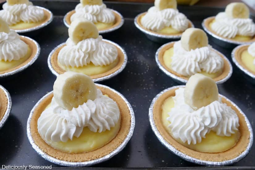 Twelve mini banana cream pies on a black surface.