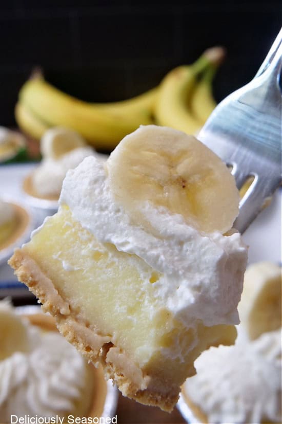 A close up of a bite of banana pie with whipped cream and a banana slice on top.
