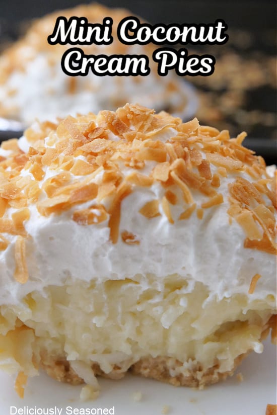A close up of a mini coconut cream pie with a bite taken out of it showing the custard filling, the whipped cream topping, and shredded toasted coconut.