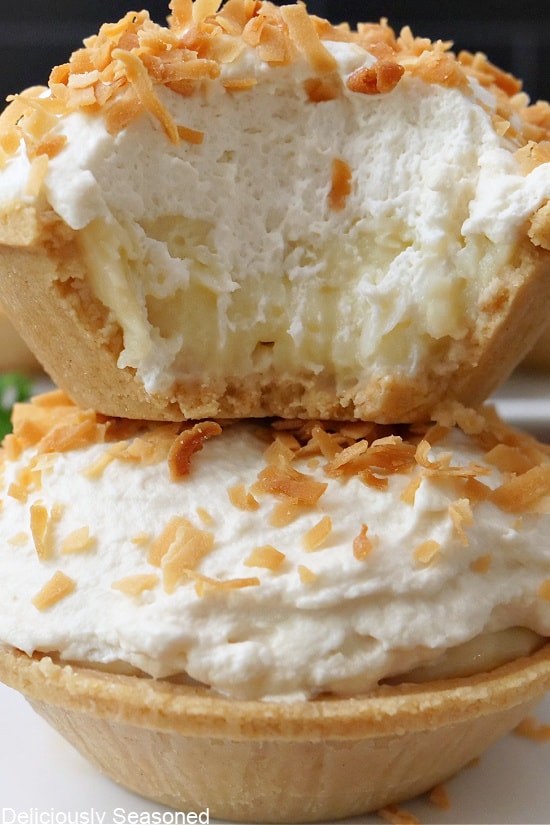 A close up of two mini coconut cream pies with a bite taken out of the one on top.