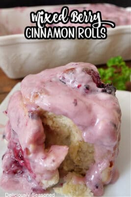 A cinnamon roll with mixed berries filling and a berry cream cheese frosting.
