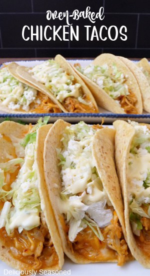 Two white plates with baked chicken tacos with lettuce, sour cream and cheese on them.