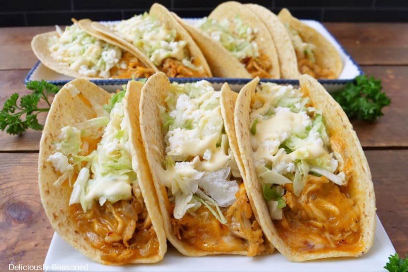 A horizontal photo of two white plates with baked chicken tacos on them.