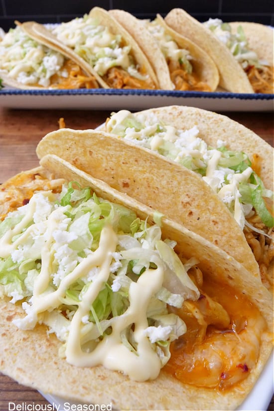 A close up photo of two baked chicken tacos on a white plate with more tacos in the background.